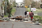 Local residents sit near debris on a road outside a hospital