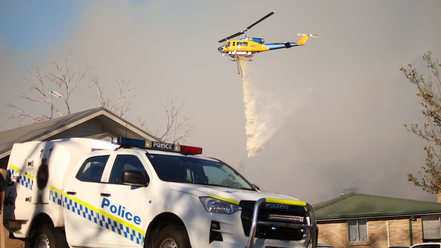 A helicopter dumps water on a fire behind a house.