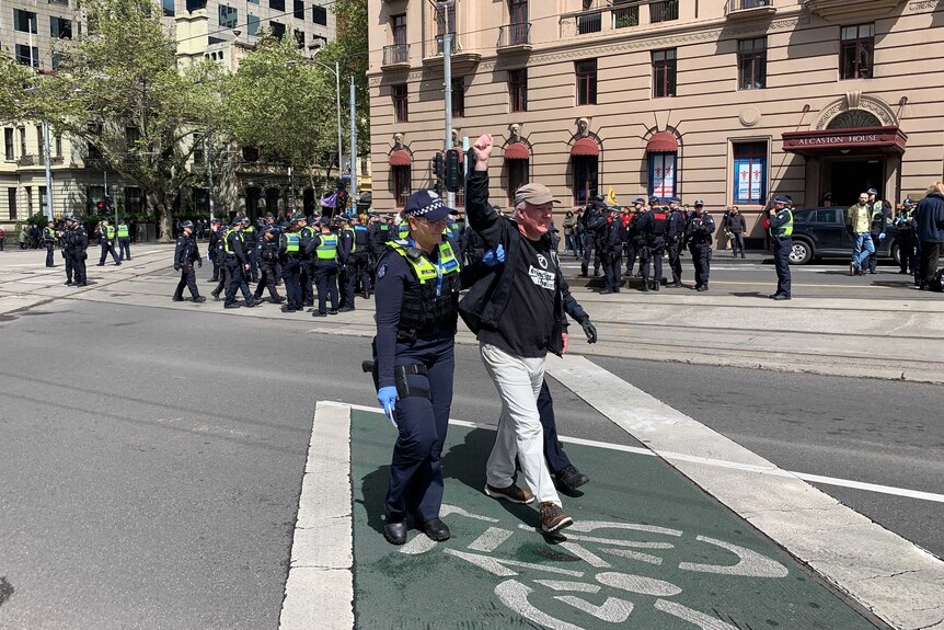 A male protester holds his hands high as he is arrested by police at a Melbourne intersection.