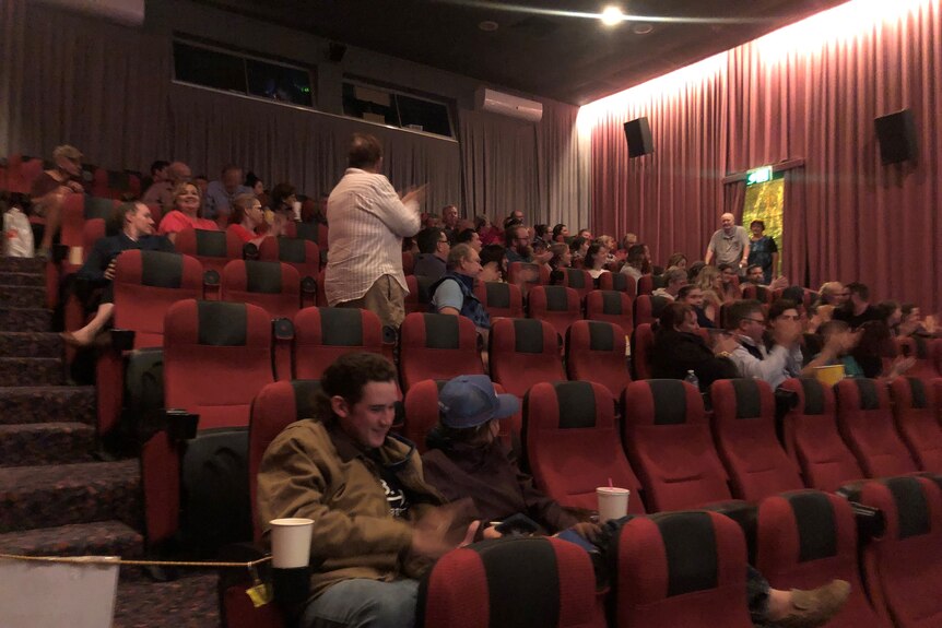A group of people sit in a movie theatre, some are clapping.