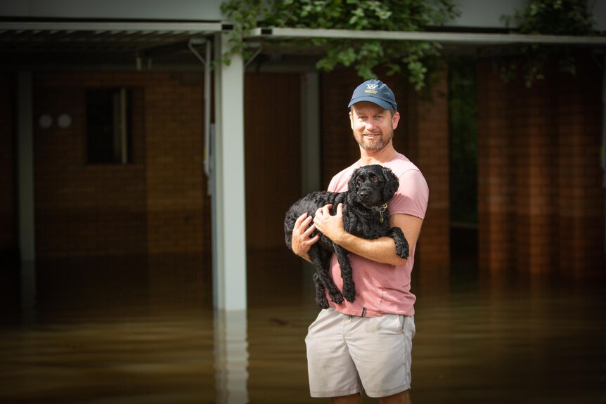 Man stands in flood waters holding dog.