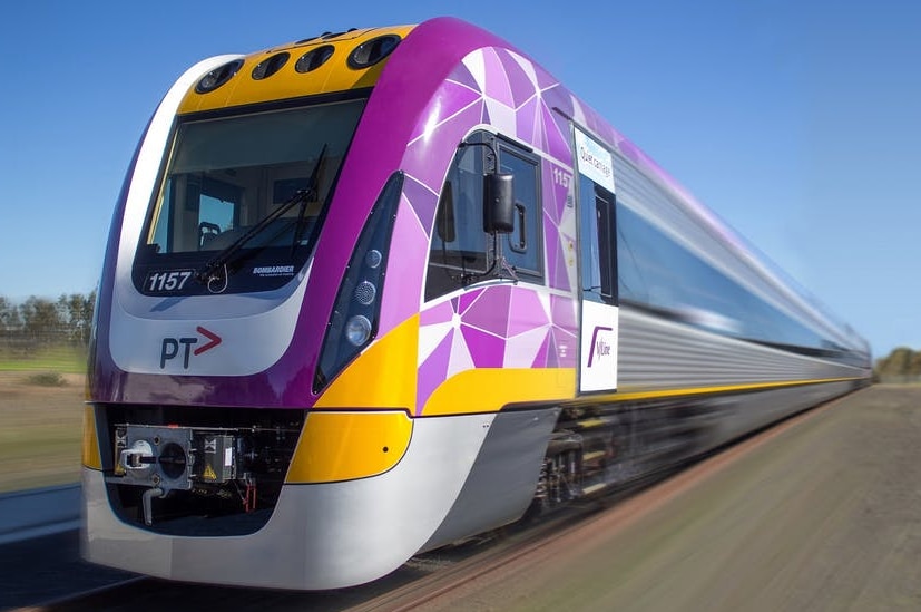 A purple, yellow and grey train moves along railway tracks in a rural setting.