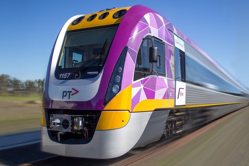 A purple, yellow and grey train moves along railway tracks in a rural setting.