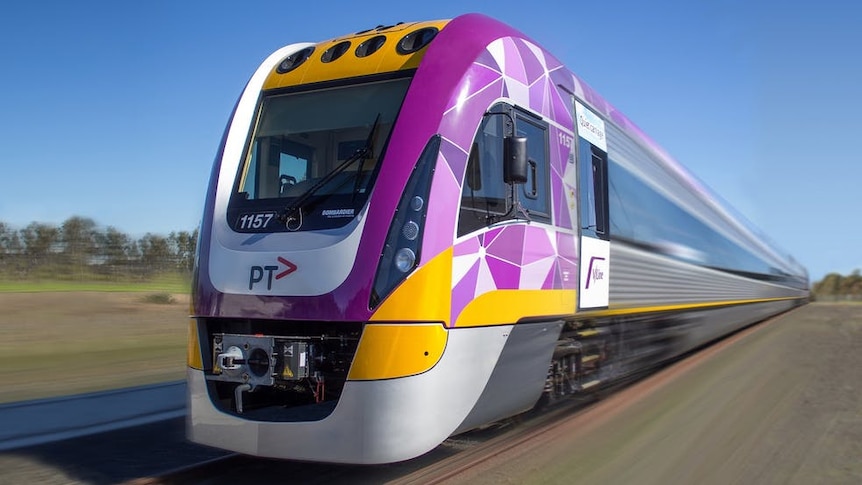 A purple, yellow and grey train moves along railway tracks in a rural setting.