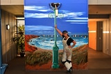 Sharron Tancred leans against a mural of a ocean scene that features a lamp post.