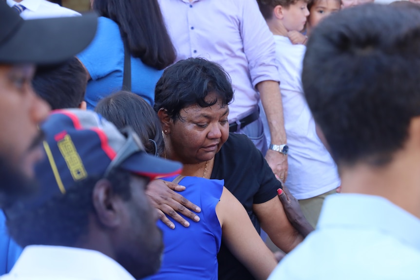 A woman hugs another woman in a crowd of people. 