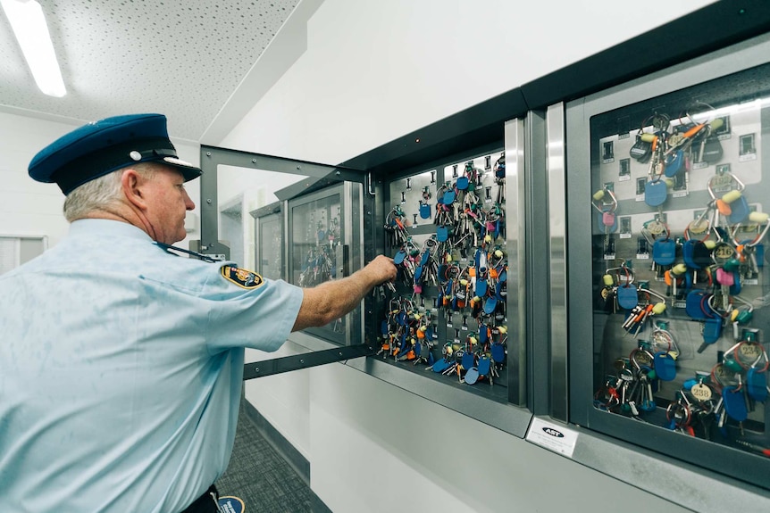 A prison guard takes a key frame a glass panel.