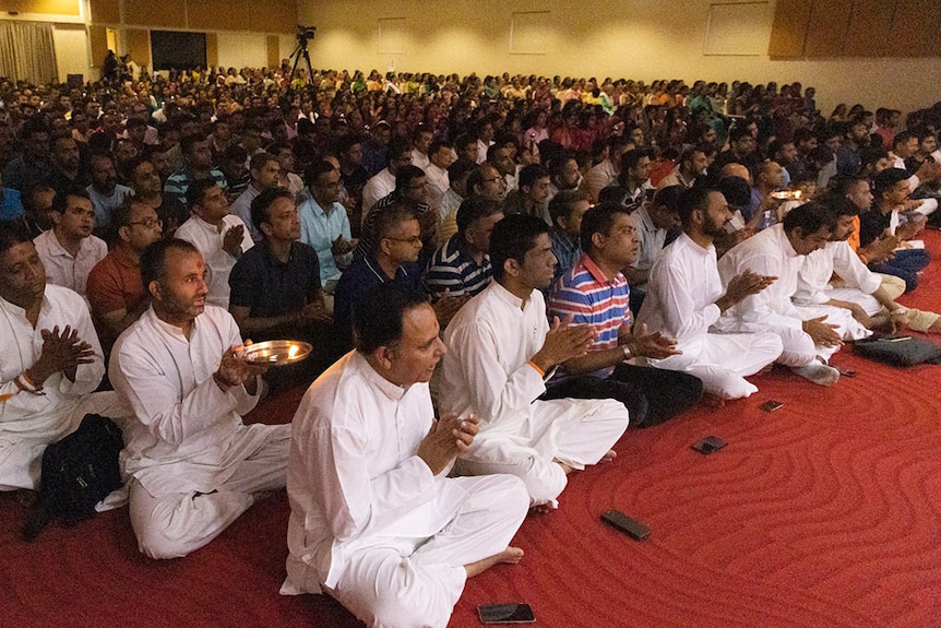 Male members of BAPS temple sitting on floor for religious assembly.