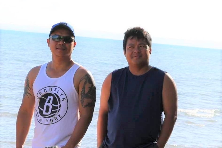 Two men standing together with an ocean view behind them