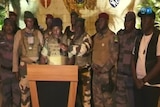 Group of men in camoflage and berets stand around podium 