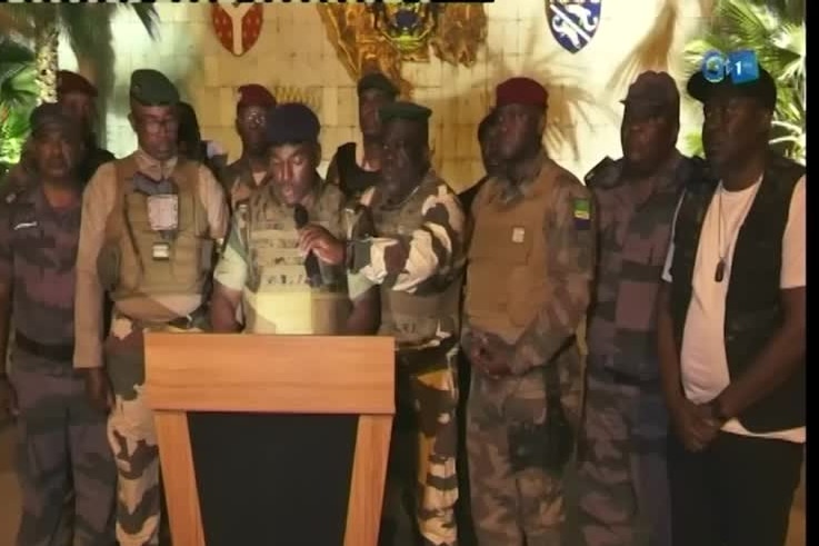 Group of men in camoflage and berets stand around podium 