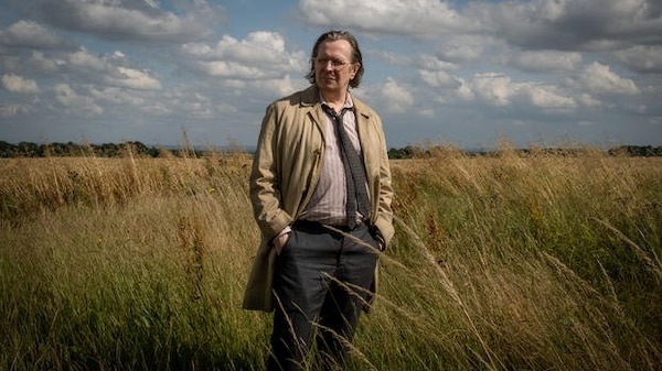 A man in a trenchcoat stands in a field.