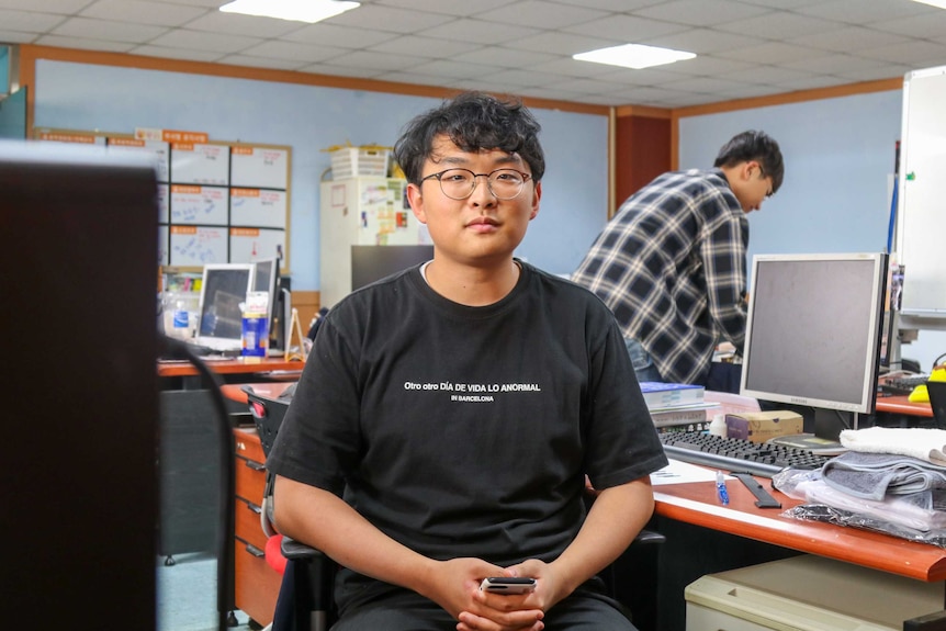 A man with glasses surrounded by desks with computers poses for the camera