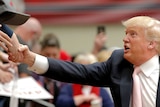 Side on view of Donald Trump reaching up to shake hands with supporters, only their arms visible.