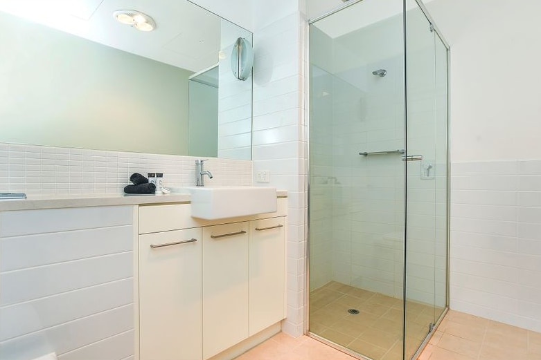 The bathroom of a home - a shower and basin can be seen. Mini toiletries and towels can be seen on the bench.