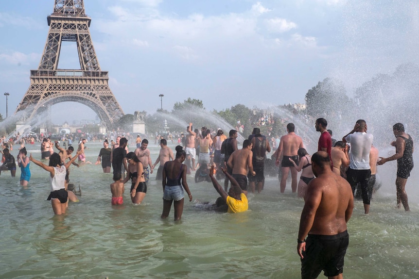Hundreds of people play in the waters of a fountain in front of the Eiffel Tower.