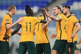 A group of Socceroos players stand on the ground, high-fiving and patting each other on the back after a goal.