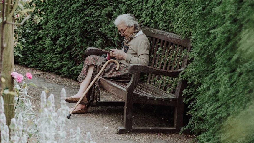An elderly woman sitting on a bench in a garden for a story about visiting loved ones who have dementia.