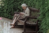 An elderly woman sitting on a bench in a garden for a story about visiting loved ones who have dementia.