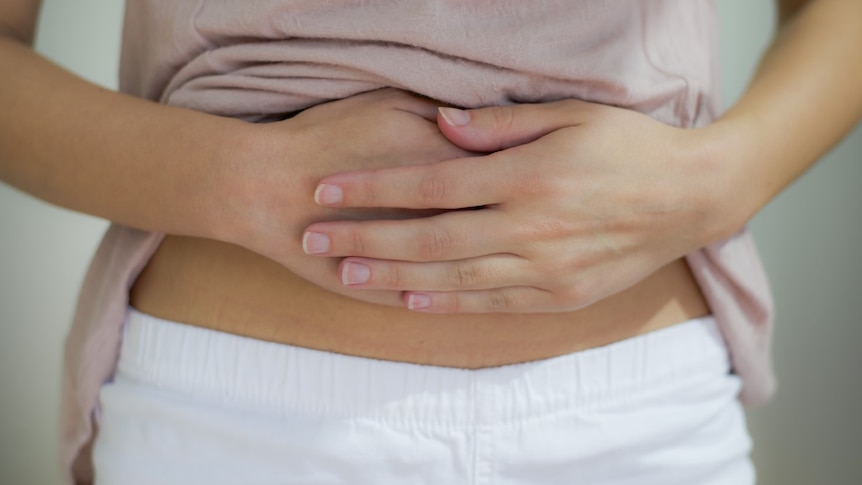 Woman has top lifted and cradles abdomen 