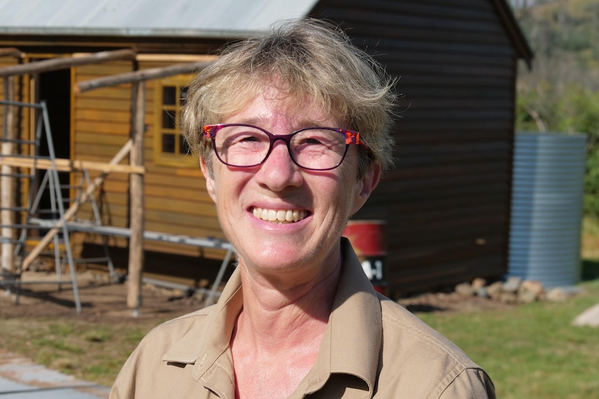 Close up of woman with short hair and a wooden hut in background