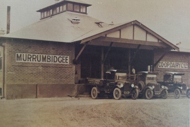 An old photo of a milk factory with old trucks out the front.