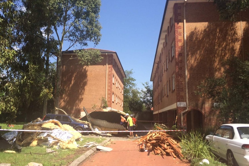 Workers inspect a roof, which blew off a building and landed on a pathway and car nearby.