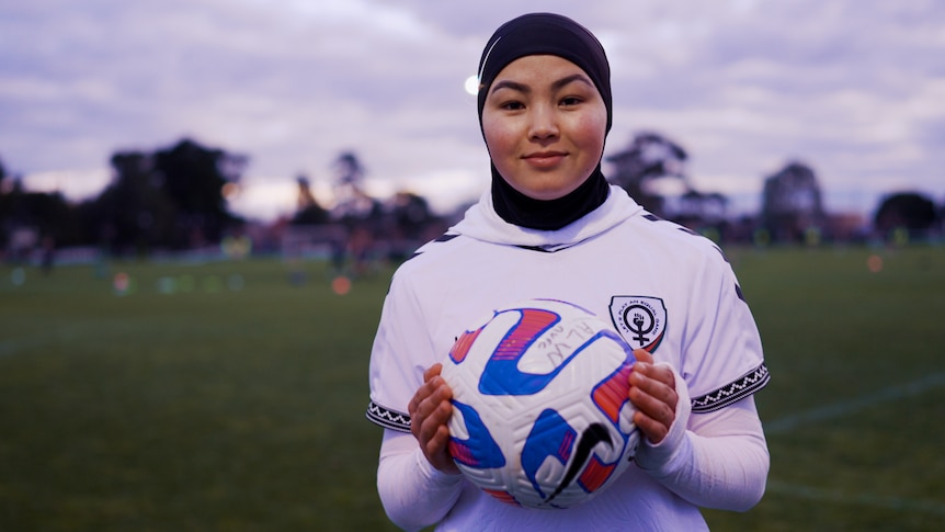 Adiba holds a soccer ball and looks at the camera standing on a Melbourne soccer pitch