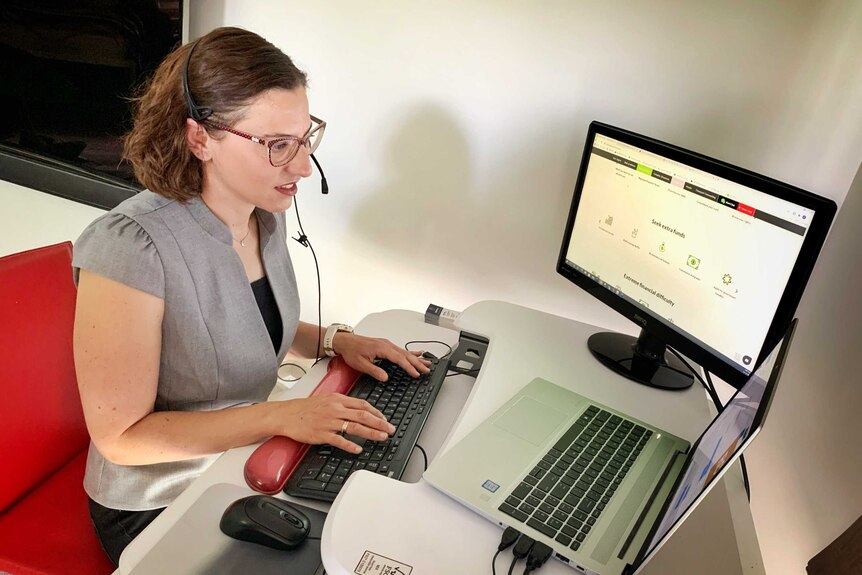 A woman types on a keyboard in front of two screens, while wearing a headset.