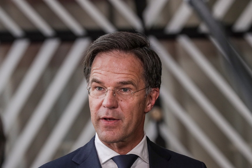 mark rutte wearing a suit and tie and glasses looks to the left of screen