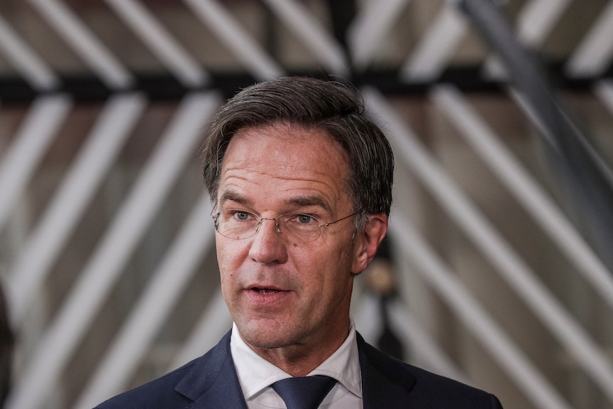 Mark Rutte in giacca, cravatta e occhiali guardando a sinistra dello schermo