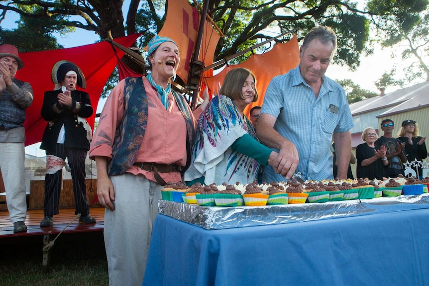 Cast members in convict costumes cut a large cake in front of a stage.