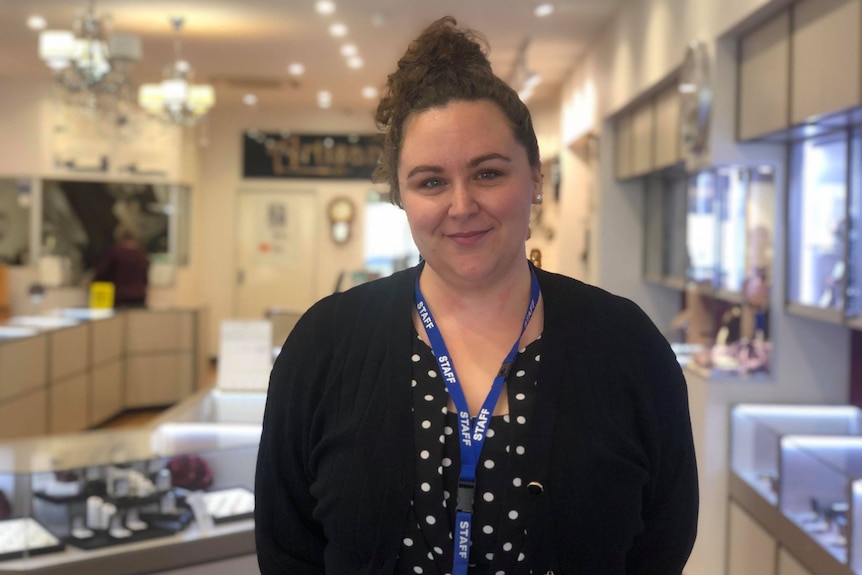 Woman with brown hair and black cardigan standing standing in front of a jewelry store