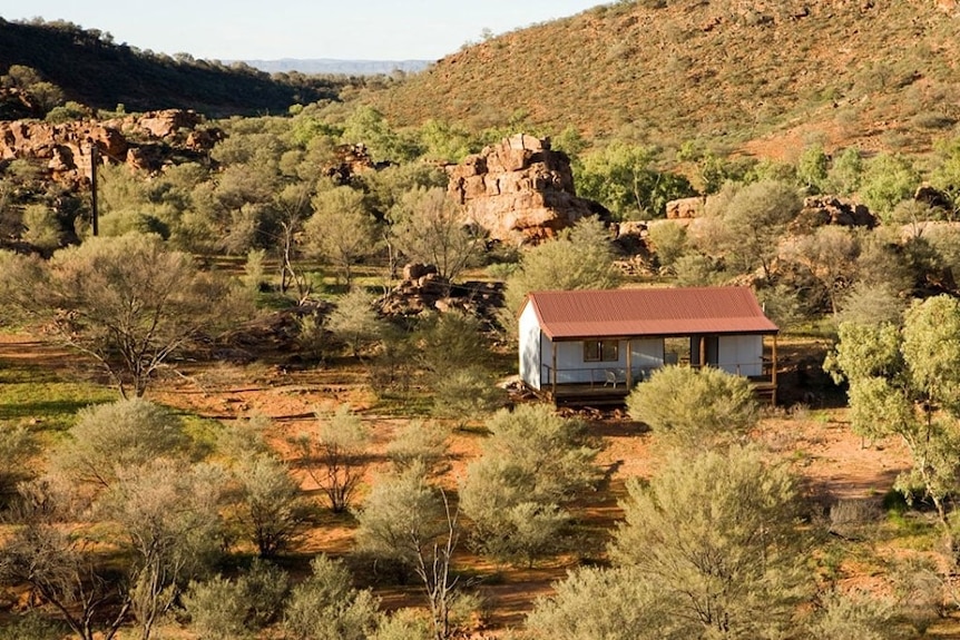 A wide angle shot of a small tin cabin nestled among trees in a rocky outback landscape.