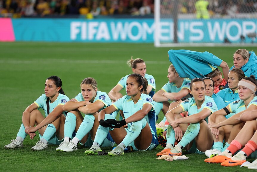 The Matildas sit together on the ground