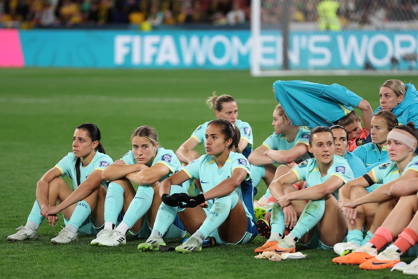 The Matildas sit together on the ground