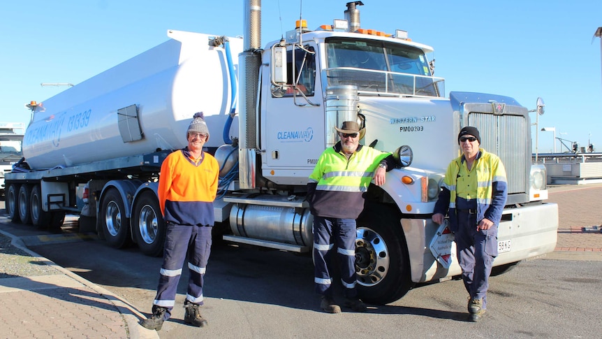 A white haulage truck with three men standing in front of it