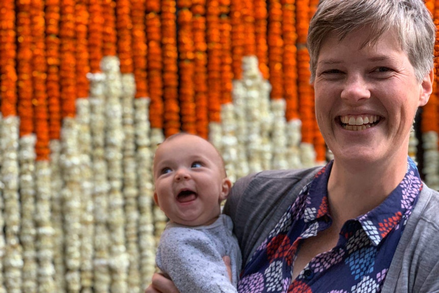 A woman holding her baby and smiling to camera