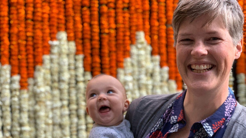 A woman holding her baby and smiling to camera