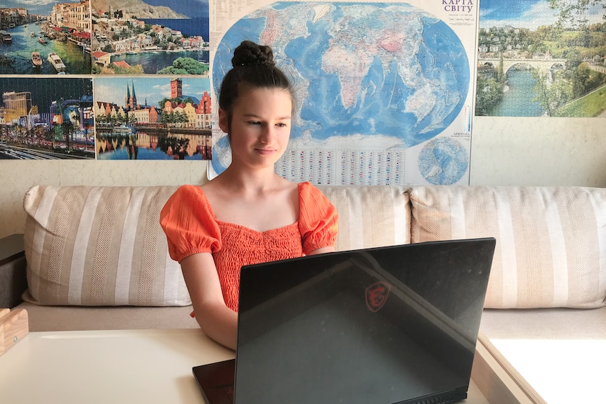 A young girl looking at something on her laptop with a poster of a world map behind her