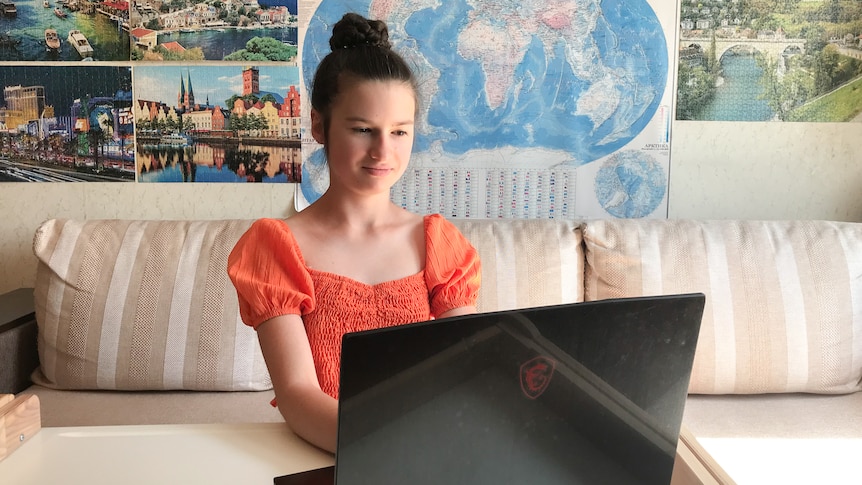 A young girl looking at something on her laptop with a poster of a world map behind her