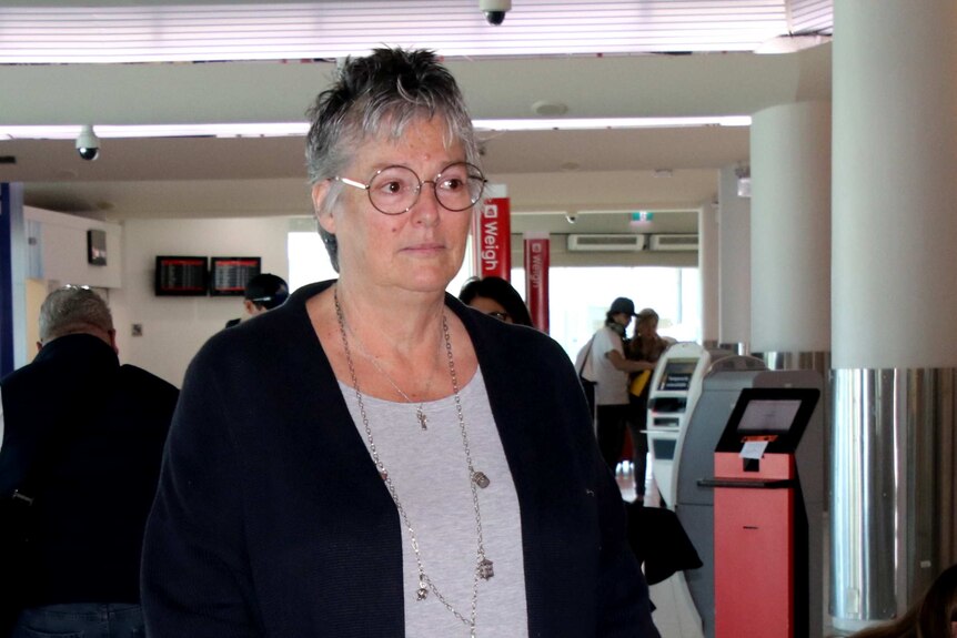 A middle-aged woman with a suitcase standing in line at an airport.