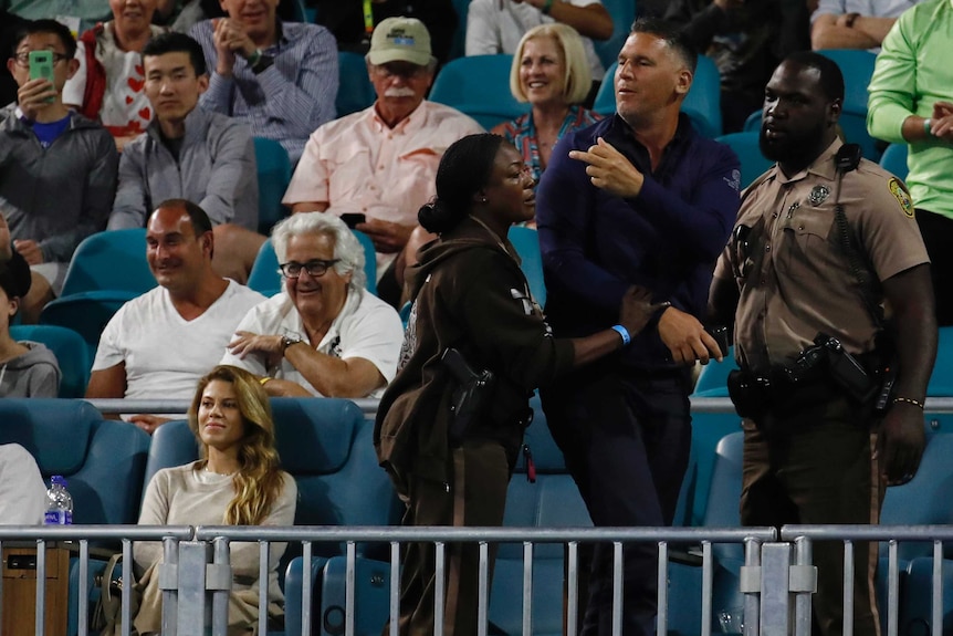 A spectator is led away by police officers as he gestures from the grandstand at Nick Kyrgios.