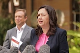 Annastacia Palaszczuk speaks in front of microphones with the health minister behind her.