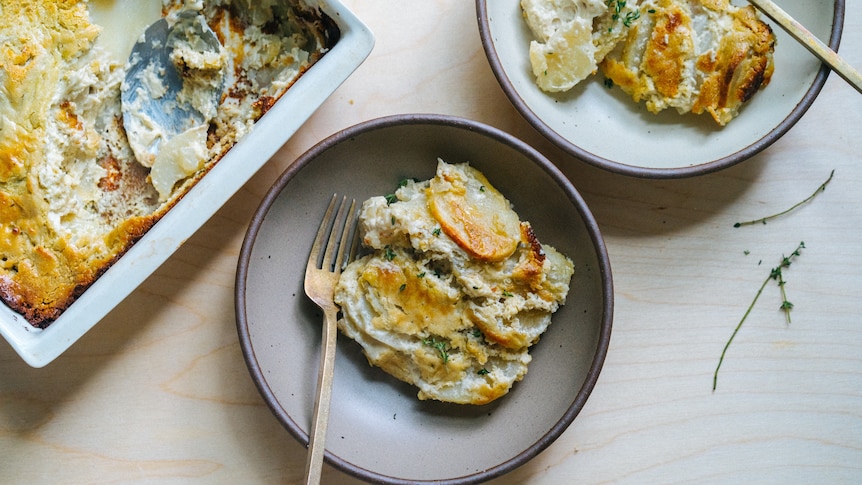 Two bowls contain serves of a creamy potato gratin, next to the oven dish they have been scooped out of.