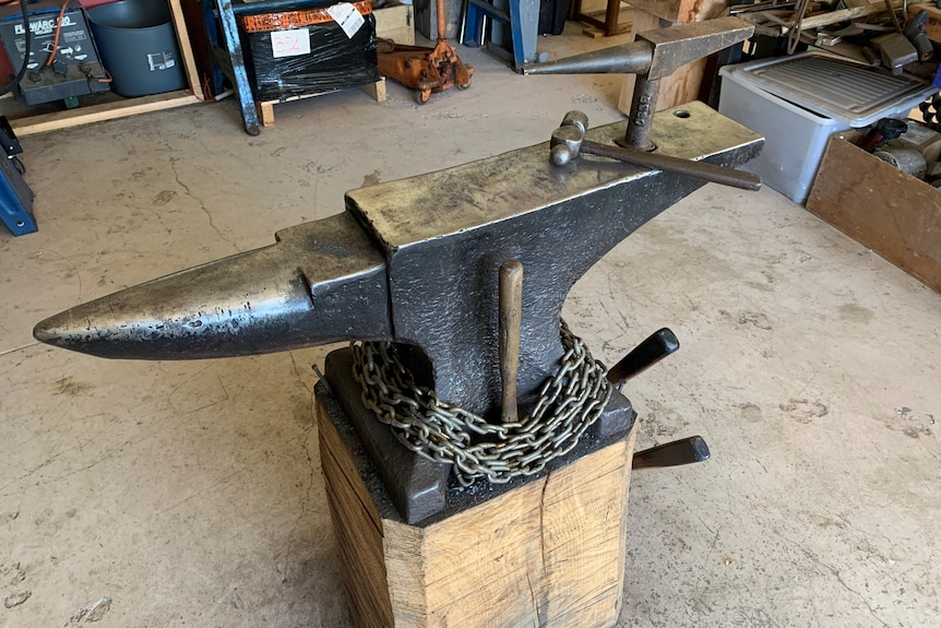 A metal anvil on a wooden block with a hammer sitting on top.