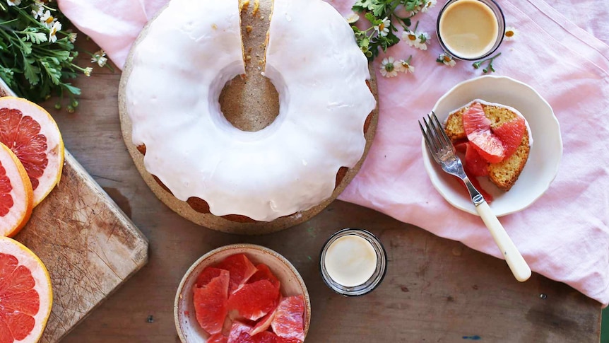 An overhead shot of a bundt cake surrounded by a plate of sliced grapefruit and coffee, illustrating our simple recipe.