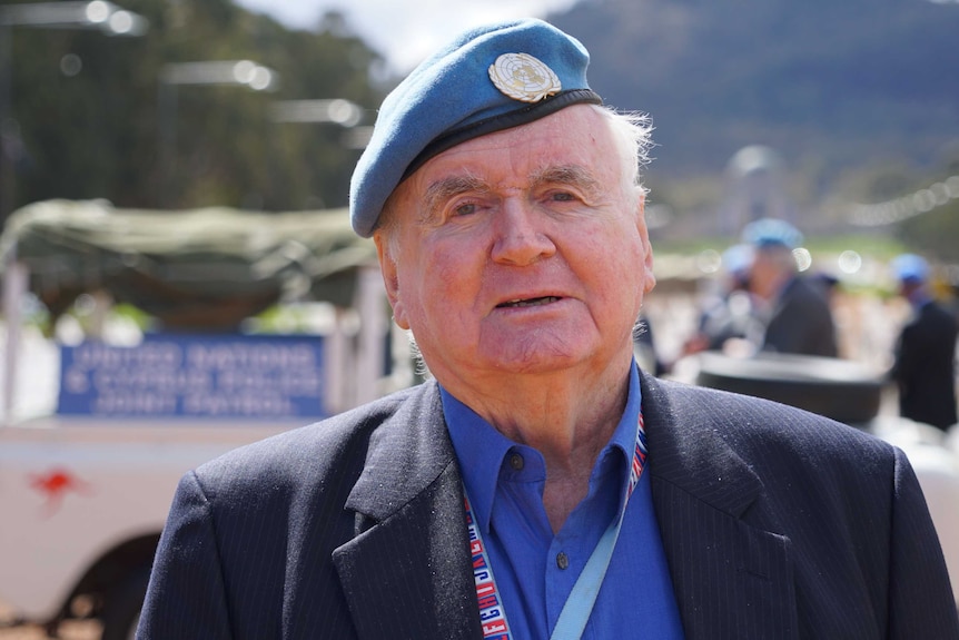 A man, wearing a blue peacekeeper beret, stands on Anzac Parade .