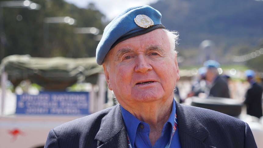 A man, wearing a blue peacekeeper beret, stands on Anzac Parade .