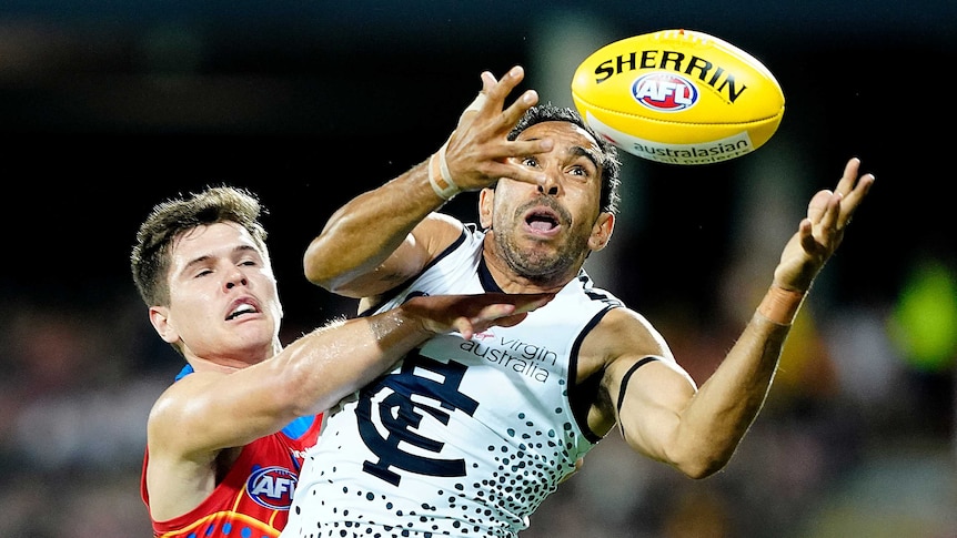 Eddie Betts holds his hands out and looks at a yellow AFL ball while being challenged by a Suns player